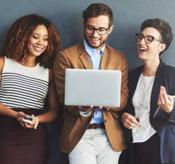 Professionals in an office looking at a laptop together and smiling